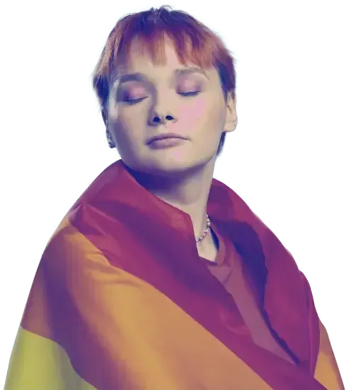 Persona con cabello pelirrojo, ojos cerrados, envuelta en la bandera del orgullo